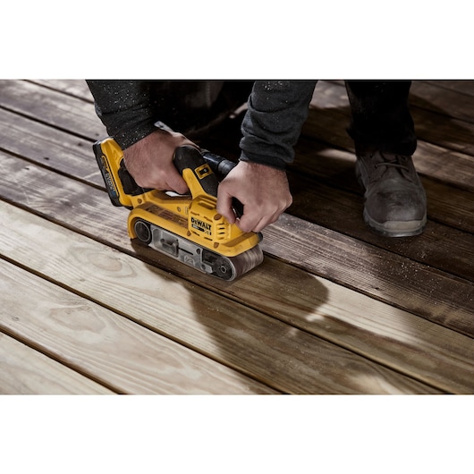 User sanding an outdoor wooden deck with the DCW220B and the DCBP520 battery attached 